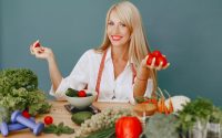 Healthy lifestyle concept with woman holding tomatoes and surrounded by fresh vegetables in a studio setting.