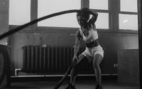 Woman in a gym engaging in vigorous battle rope workout for fitness.
