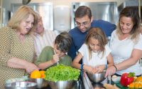 Family of various ages gathers in kitchen to cook meal together, showcasing culinary togetherness.